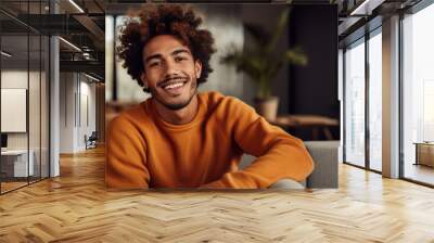 Portrait of a smiling man with curly hair wearing a rust-colored sweater, looking directly at the camera, with a warm and friendly expression Wall mural