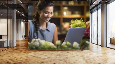 Portrait of woman entrepreneur sitting in own flower shop, working on laptop. Wall mural