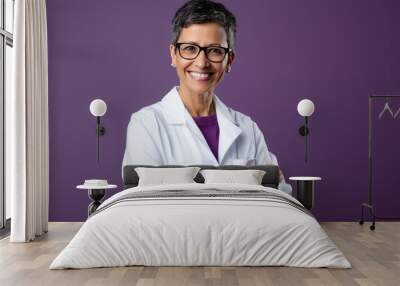 Professional woman with short hair wearing glasses and a white lab coat , smiling confidently with her arms crossed, against a colored background. Wall mural