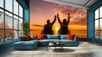 Silhouette Disabled handicapped young man in wheelchair raised hands with his Disabled friend in sunset. Wall mural