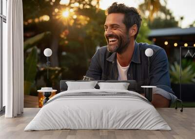 Smiling man sits at a table during an outdoor evening party in a home's backyard Wall mural