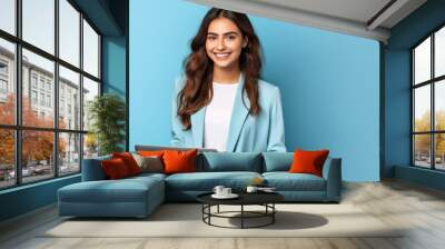 Smiling woman holding a laptop against a blue background. Wall mural