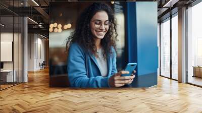 Smiling woman in blue clothes is using the phone outdoors Wall mural