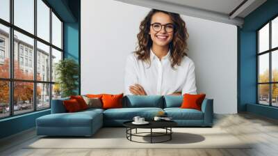 Smiling woman with curly hair and glasses, wearing a white shirt, against light grey background Wall mural