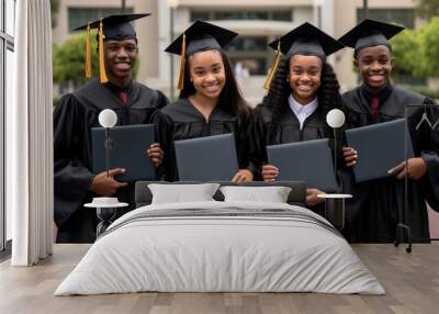 Successful graduates in academic dresses are holding diplomas and smiling outdoors Wall mural