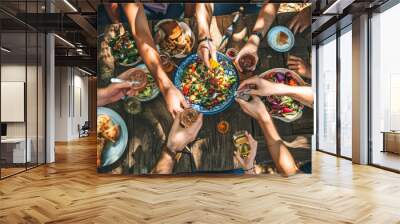 Top view of a group of people sitting around a rustic wooden dining table, toasting with their glasses raised amidst a spread of various dishes Wall mural