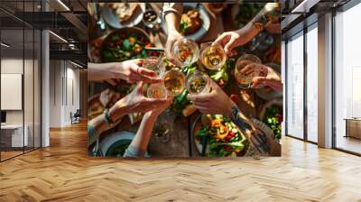 Top view of a group of people sitting around a rustic wooden dining table, toasting with their glasses raised amidst a spread of various dishes Wall mural