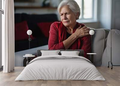 Woman with shoulder and neck pain sits on the couch at home Wall mural