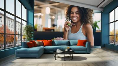 Young athletic woman eats a salad in her plate while eating breakfast Wall mural