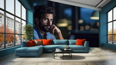 Young businessman deep in thought with a hands on his chin while working on a laptop in a modern office.Created with Generative AI technology. Wall mural