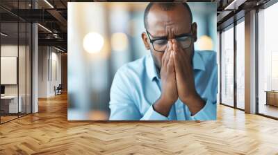 young man with his eyes closed, holding his temples as if experiencing a headache or stress. Wall mural