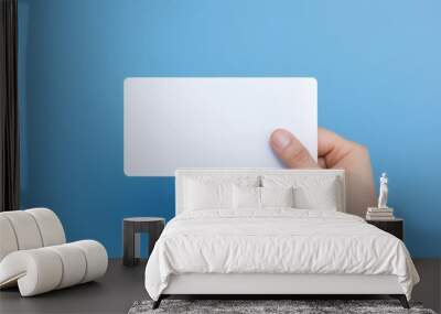 Hand is holding blank white card on a blue. Woman holding blank business card on blue background Wall mural