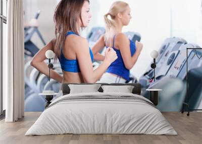 Two young women run on machine in the gym Wall mural