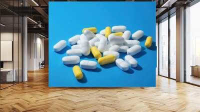 Collection of white, blue and yellow pills on blue background Wall mural