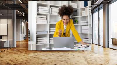 Beautiful African American black businesswoman working with laptop computer and financial documents at table in office typing documents, checking email, joining online meeting at work Wall mural