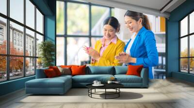 Two Asian businesswomen are deeply engaged in a discussion about data analysis work on a computer screen with graphs and charts. Showcase teamwork Wall mural