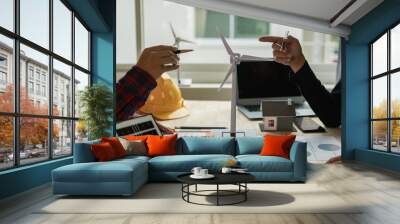 Two Caucasian engineers and architects work together in office with wind turbine and solar panels on table, renewable energy installation concept Wall mural