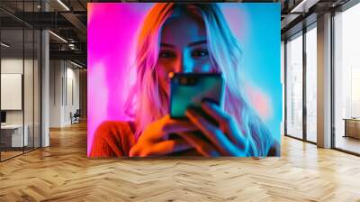 A young woman enjoying her mobile phone in vibrant neon light, highlighting modern technology and casual lifestyle. Wall mural