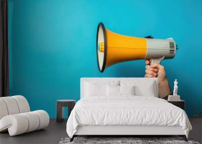 Hand holding a bright yellow megaphone against a blue background Wall mural