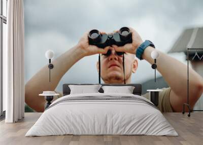 The young man is scrutinizing something through binoculars. Wall mural