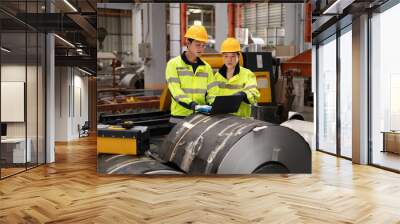 Two male engineers in uniforms and caps using laptop checking machinery system in factory. Industrial factory workers. Machinery maintenance technician working concept. Wall mural