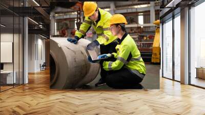 Two male engineers in uniforms and caps using laptop checking machinery system in factory. Industrial factory workers. Machinery maintenance technician working concept. Wall mural