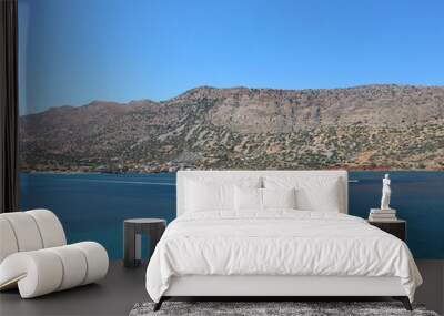 Blue ocean with two jet skis riding across the water. Mountain in the background with some grass and bright blue sky. Small houses in the distance. Greece Spinalonga Wall mural