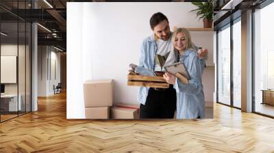 Young happy couple in room with moving boxes in new home, husband hugging wife celebrating mortgage Wall mural