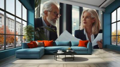 Two professional executives discussing financial accounting papers working together in office. Mature business woman manager consulting older man client holding legal documents at meeting Wall mural