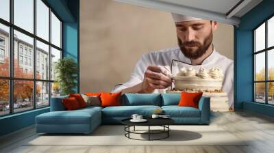 Male chef in a white uniform decorating a cake, soft beige background Wall mural