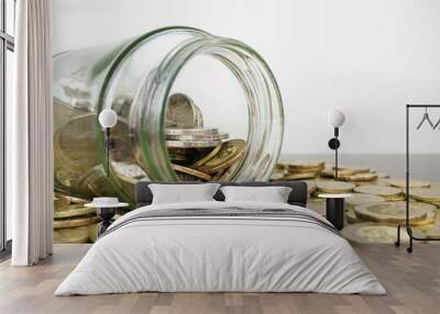 glass bottle surrounded by coins on wooden desk against white background. copy space. selective focus Wall mural