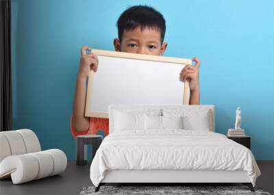 Cute little Asian boy holding a blank board, covering half of his face, isolated on blue background. Space for text, copy space, mockup banner Wall mural