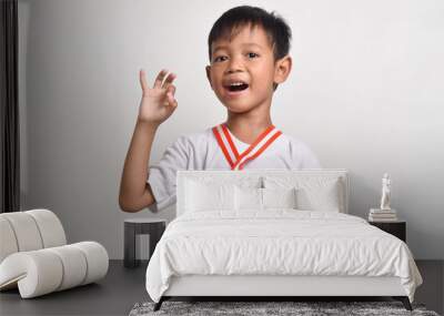 Little asian boy wearing a gold medal of an award competition. Smiling child celebrating his success, isolated on a white background with an okay sign with fingers, excellent symbol Wall mural