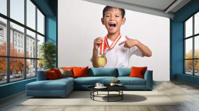 Little asian boy with a surprised expression, finger showing his gold medal isolated on a white background. The smiling child celebrating his success Wall mural