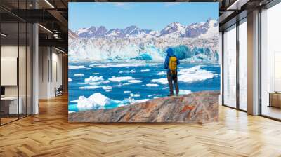 Environmental Concept - A Man Hiker looking at melting glacier - Melting of a iceberg and pouring water into the sea - Greenland - Tiniteqilaaq, Sermilik Fjord, East Greenland Wall mural