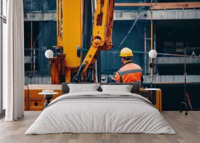 Construction worker in a yellow hardhat operating a crane on a building site. Wall mural