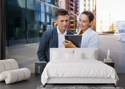 A businesswoman enthusiastically shares a digital tablet with a colleague outside a modern office building. Wall mural