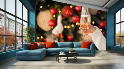 a glass of wine with champagne in hand, new year lights shining brightly rays from the garland. background texture of Christmas lights on a holiday tree. make a wish. black gift box with a bow. Wall mural