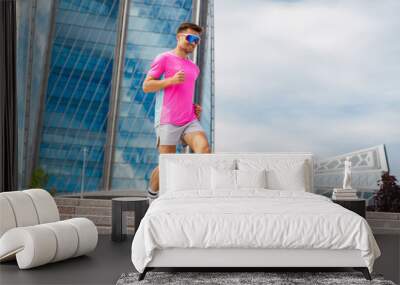 Active Male Runner in Bright Pink Shirt Descends Steps Near Modern Architecture on a Cloudy Day in the City Wall mural