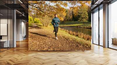 Athlete training every day in winter. Beautiful bright autumn colors. A man in warm sports clothes and thermal underwear runs fast in the autumn park. Wall mural