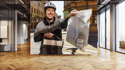 Passes the order, a male cyclist in a helmet delivers clothes in a bag to the address of the client. Wall mural