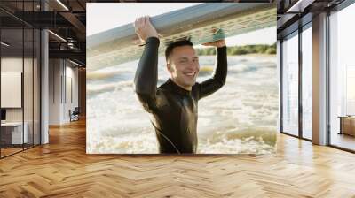 Portrait of a smiling man surfer in a wetsuit on the waves at sunset in the sea Wall mural