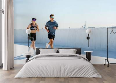 Two runners stride confidently on a rooftop track, radiating fitness and determination under clear skies. Wall mural