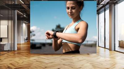 Uses a watch on her hand for training, a sporty woman does fitness exercises on the street. Wall mural