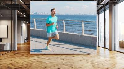 Young Man Jogging Along the Waterfront Promenade on a Sunny Day With City Skyline in the Background Wall mural