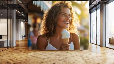 A beautiful woman with wavy hair walks on the beach on a summer day, laughing and holding an ice cream Wall mural