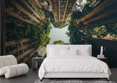 A city with many tall buildings is seen from below. The buildings are so tall that they seem to reach up to the sky. The city is surrounded by green trees and plants, making it a beautiful sight. Wall mural