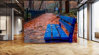 Vibrant blue park bench on a wet autumn day surrounded by fallen leaves Wall mural