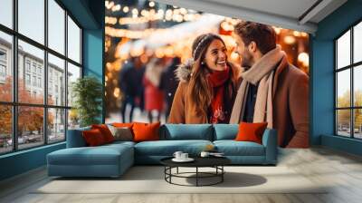 A young cheerful couple having a walk with hot drinks, dressed warm, looking at each other and laughing, snowflakes all around. Enjoying Christmas Market Wall mural