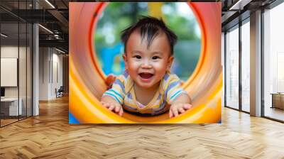 Joyful little Asian boy having fun playing on the tube slide in an outdoor playground. Wall mural